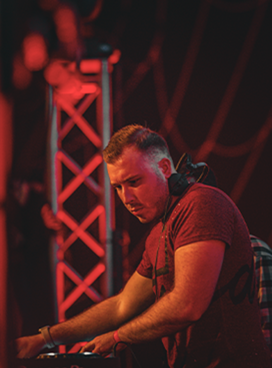 DJ wearing headphones focused on mixing music at a club with red lighting.