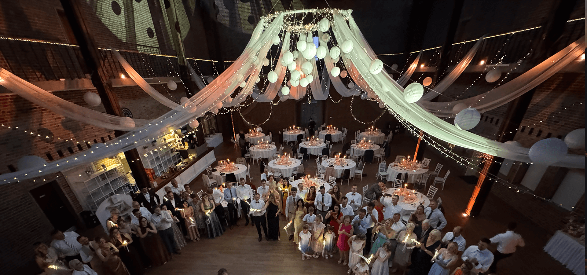 Overhead view of a wedding reception in a decorated hall with guests holding sparklers around a dance floor.