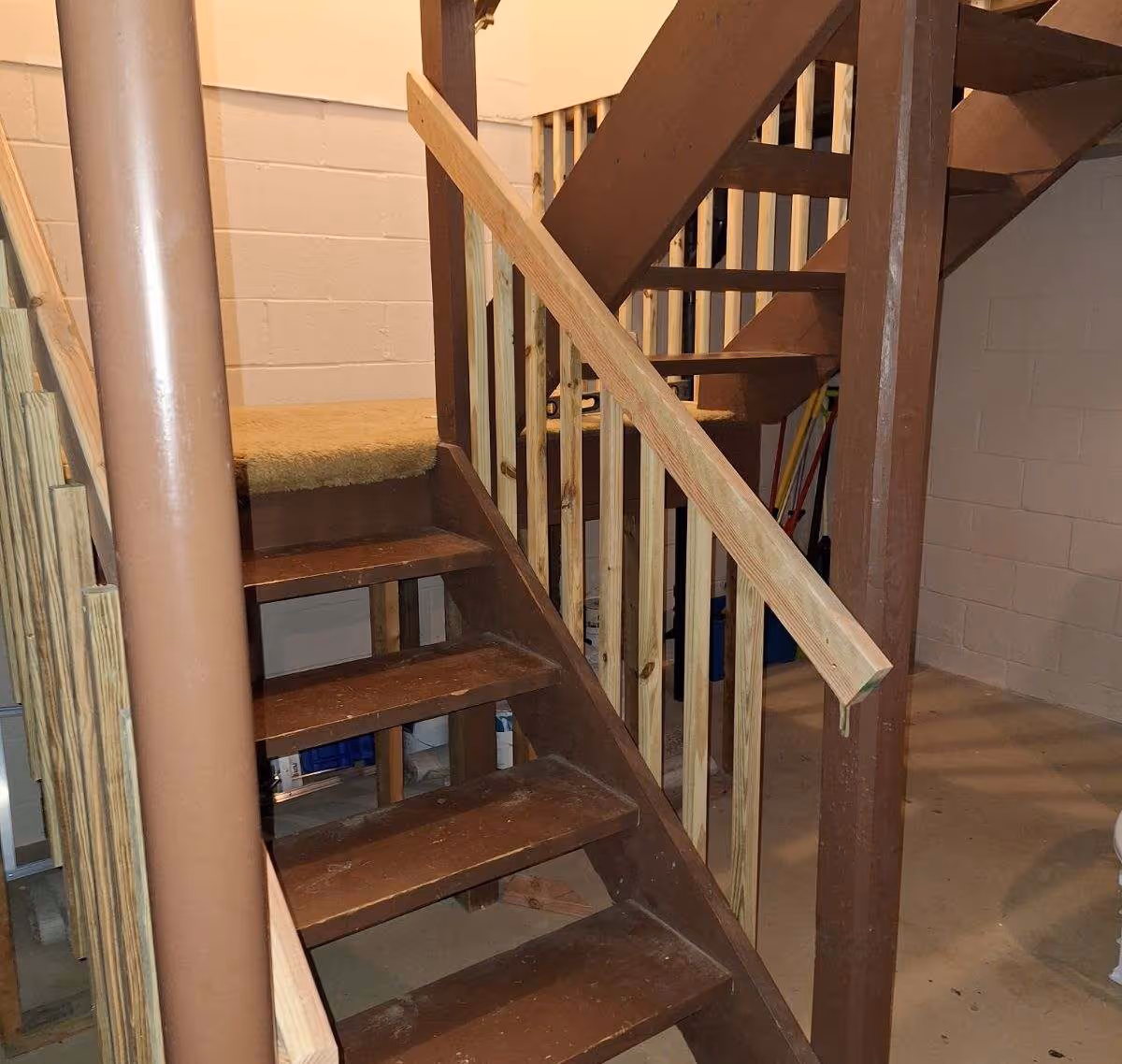 unfinished brown wooden staircase with exposed railings and a support post in a basement space