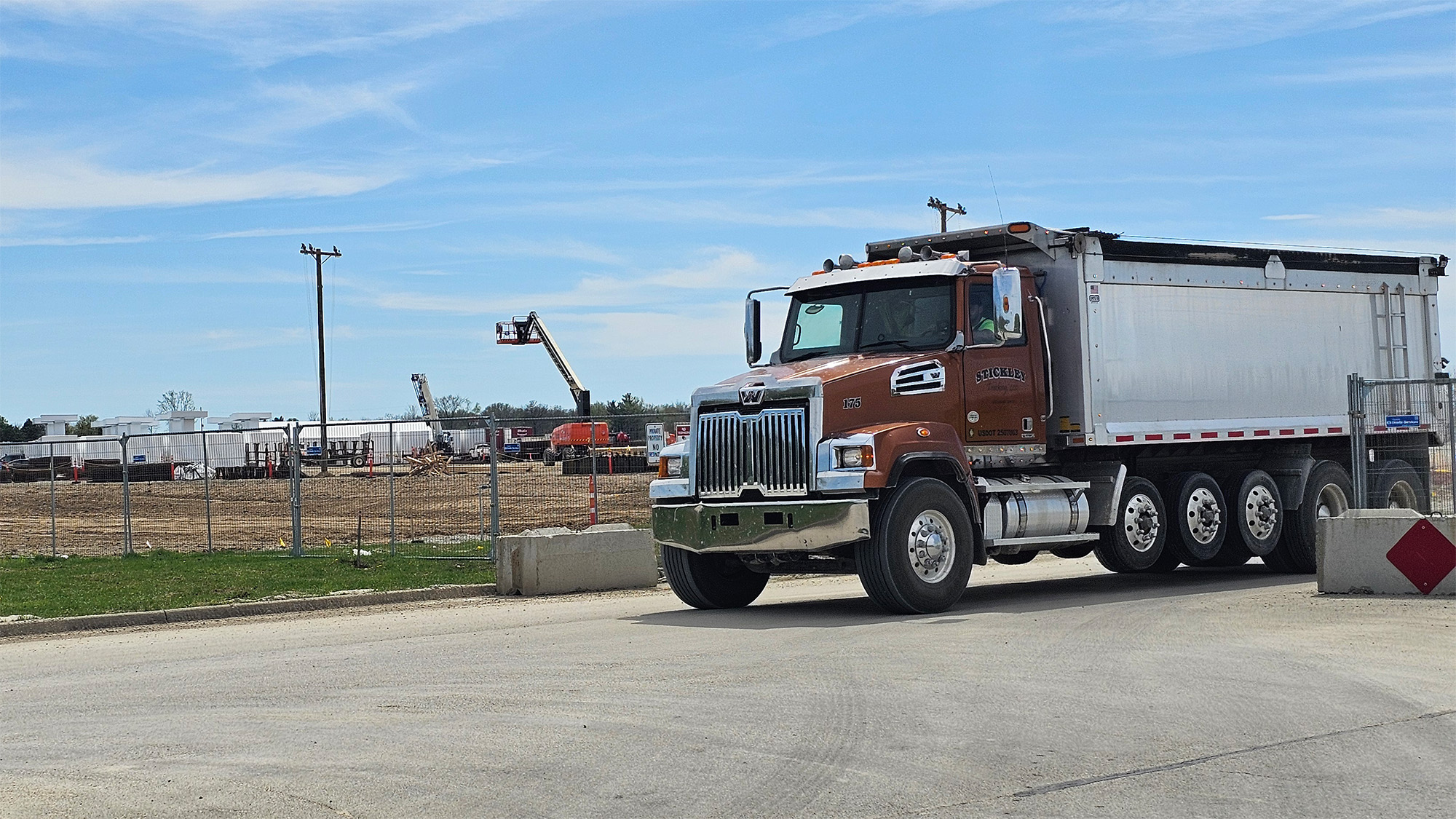 A dump truck on the road, near a job site.