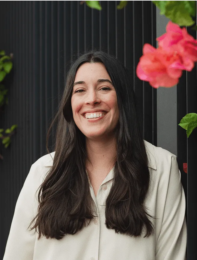 Image of Mel standing in front of a dark wall with a pink flower next to her