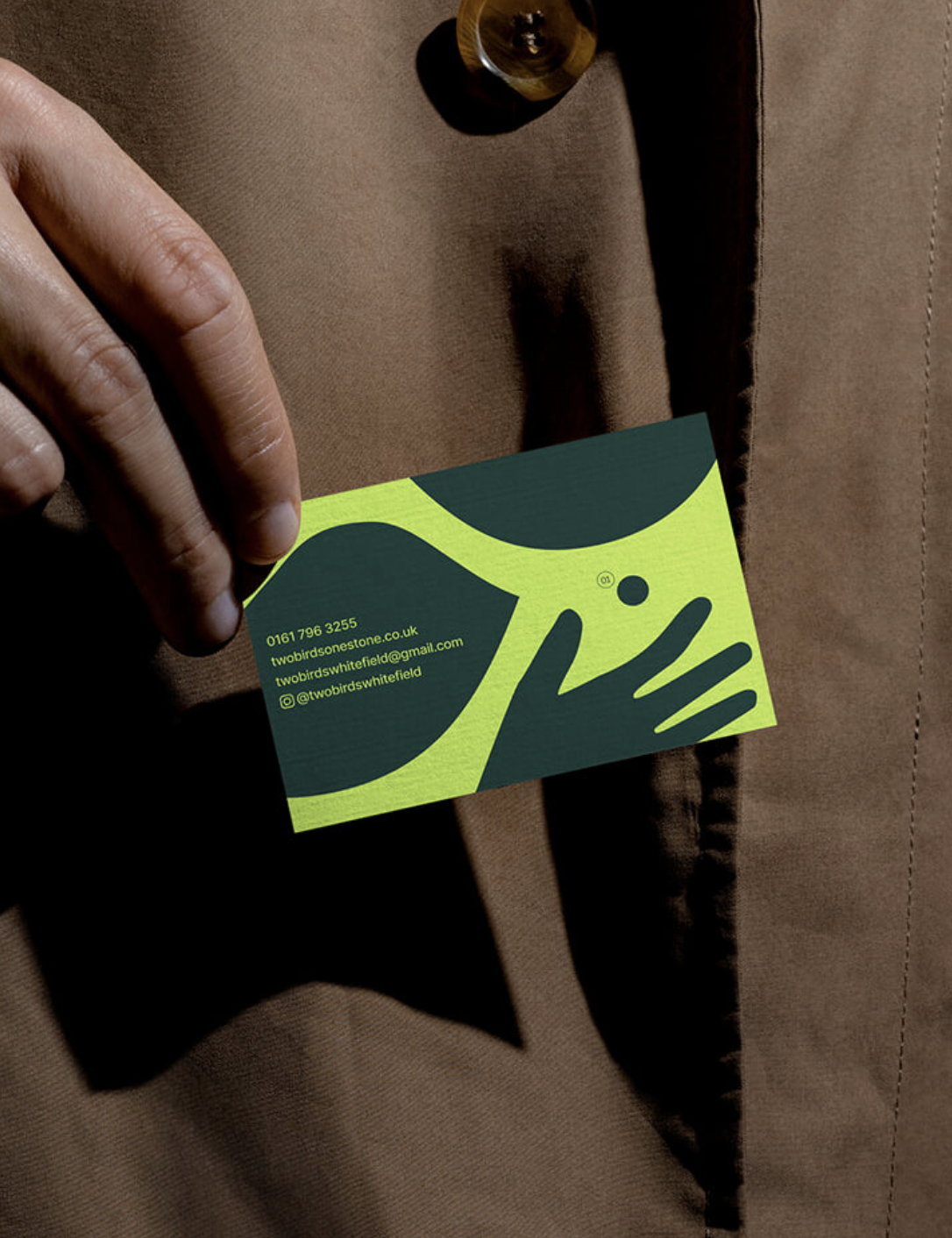 Hand holding a business card for two birds & one stone that is brightly coloured and shows information