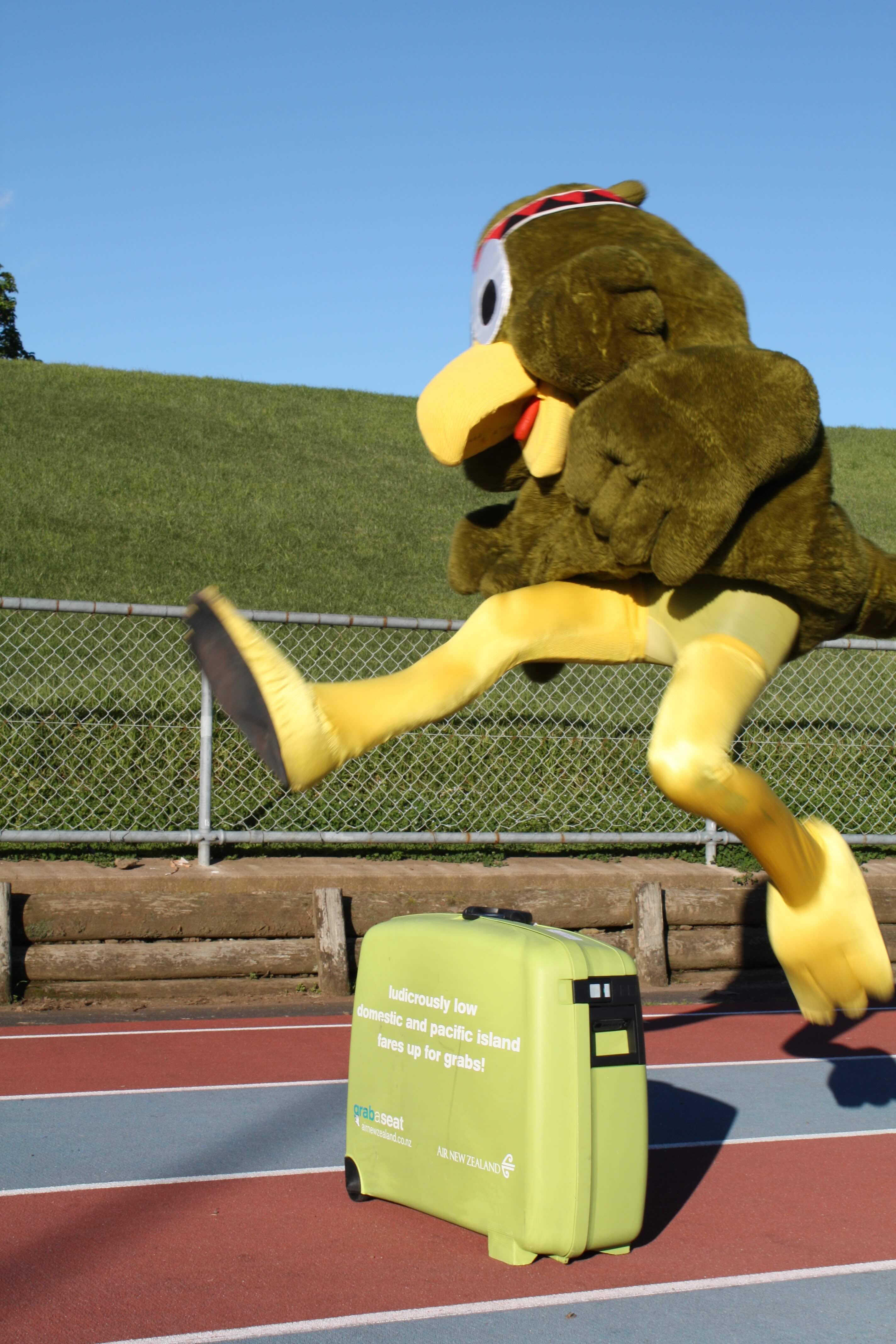 A person in a bird mascot costume jumping over a suitcase