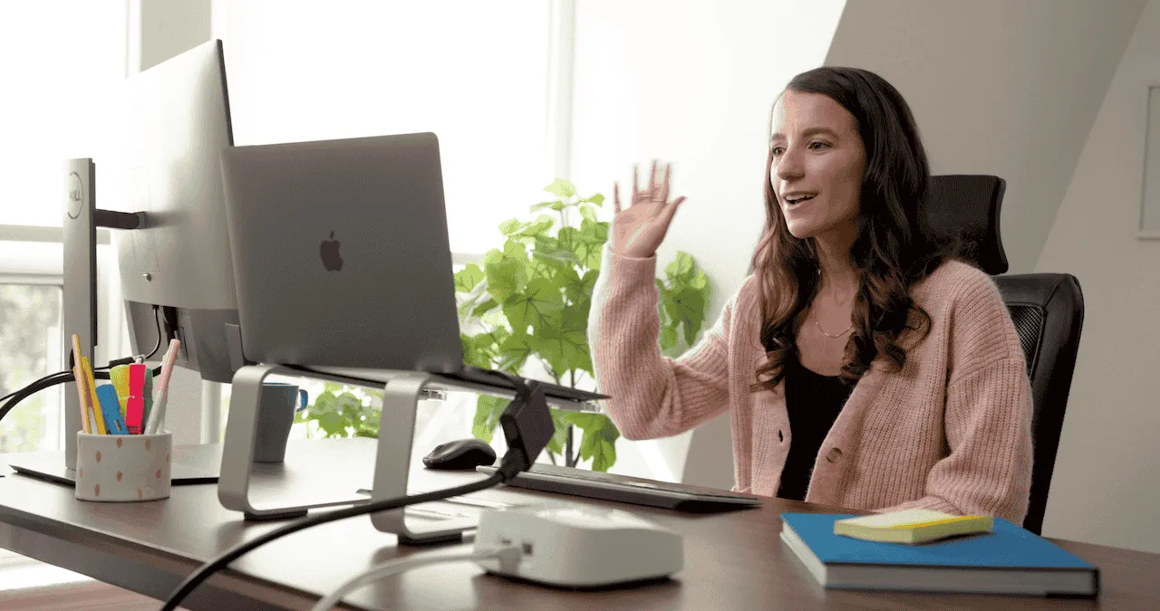 A woman sitting at a desk with her hands raised, appearing engaged or excited during a discussion or presentation.