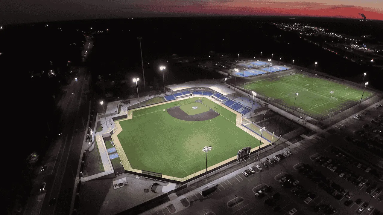 Aerial view of a baseball field illuminated at night, showcasing the diamond and surrounding stands under a dark sky.