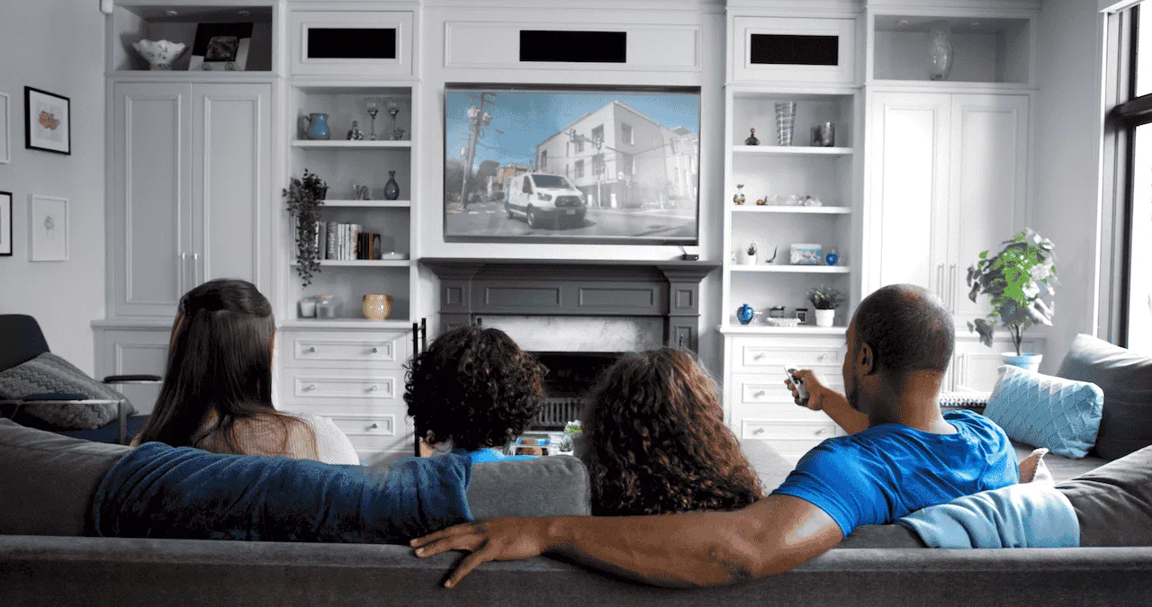 A family of four sitting together on a couch, watching television in a cozy living room setting.