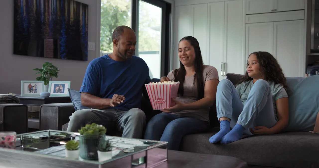 A cheerful family relaxing on a couch, sharing a bowl of popcorn while watching television.