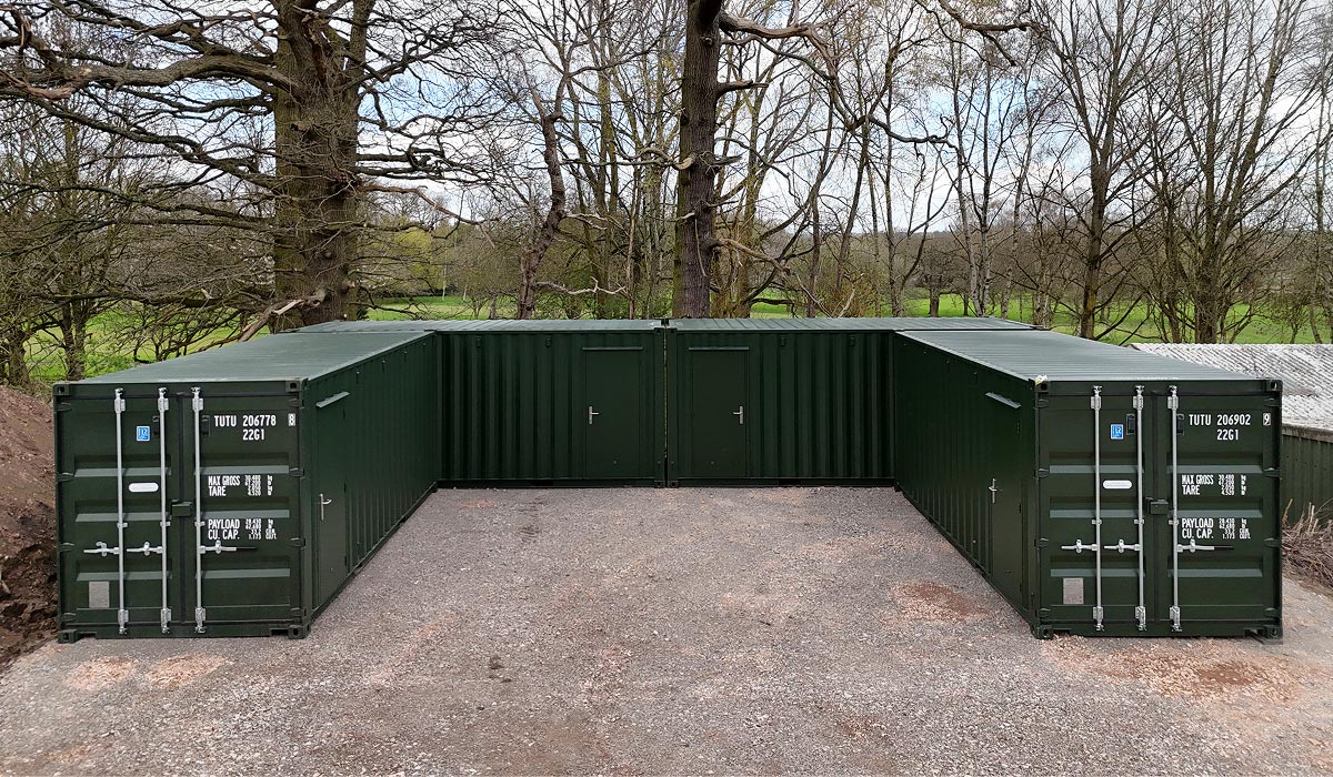 Completed greenkeeping storage compound of green converted shipping containers with access doors, set among trees at a golf club