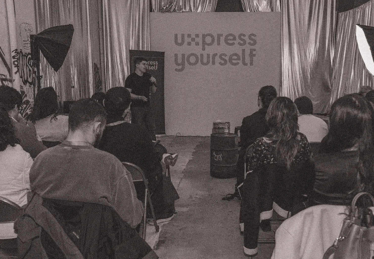 Audience seated and listening to a speaker on stage with a backdrop reading 'u:xpress yourself'.