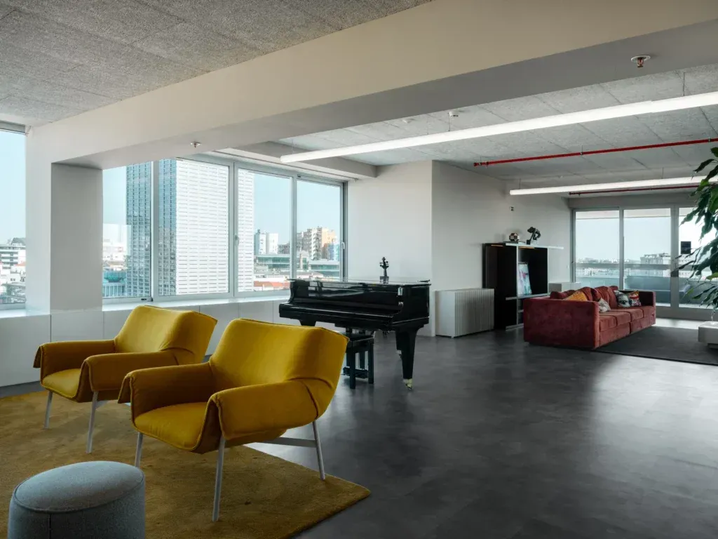 Modern living space with two yellow chairs, a black grand piano, and a red sofa near large windows.