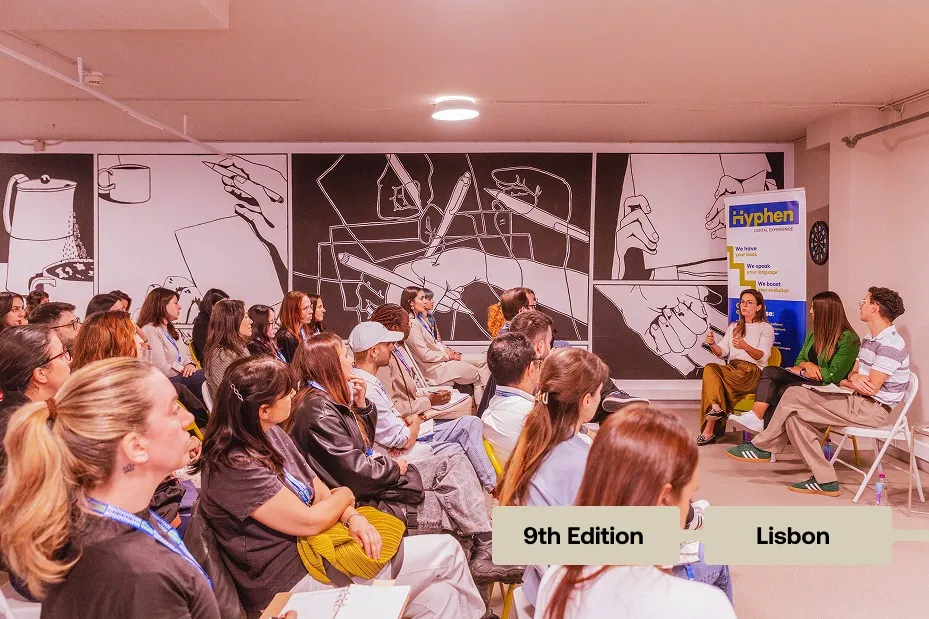 Audience listening to a speaker in a room decorated with black and white hand drawings, event in Lisbon.