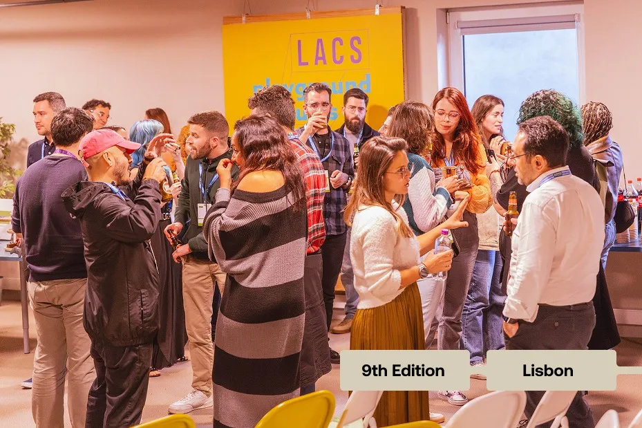 A group of people socializing and drinking in a bright room with a yellow LACS sign in Lisbon event.