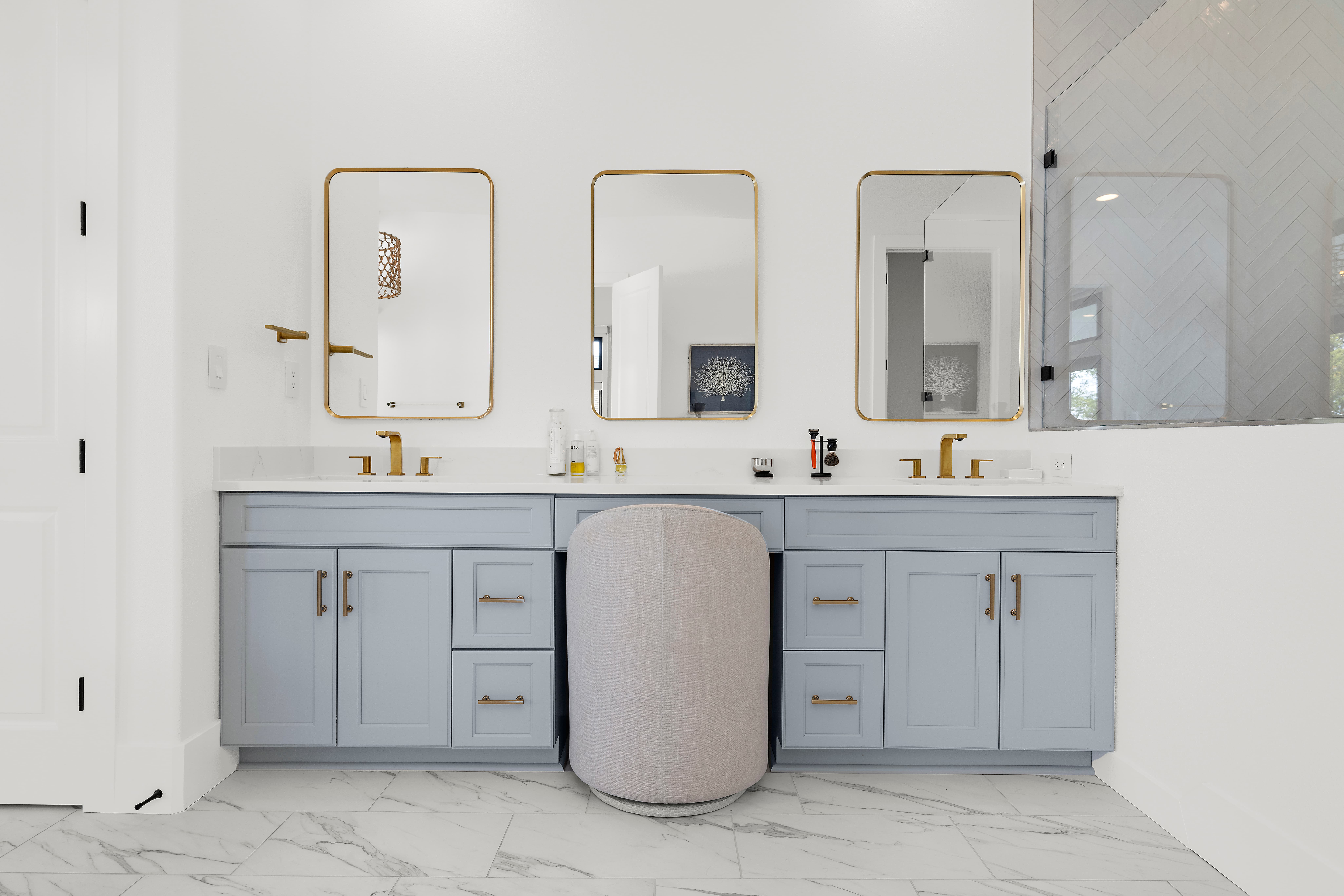 Cadle Creek - Rhode River completed home showing wide view of primary bathroom double-vanity, with chair in center, and three mirrors above.