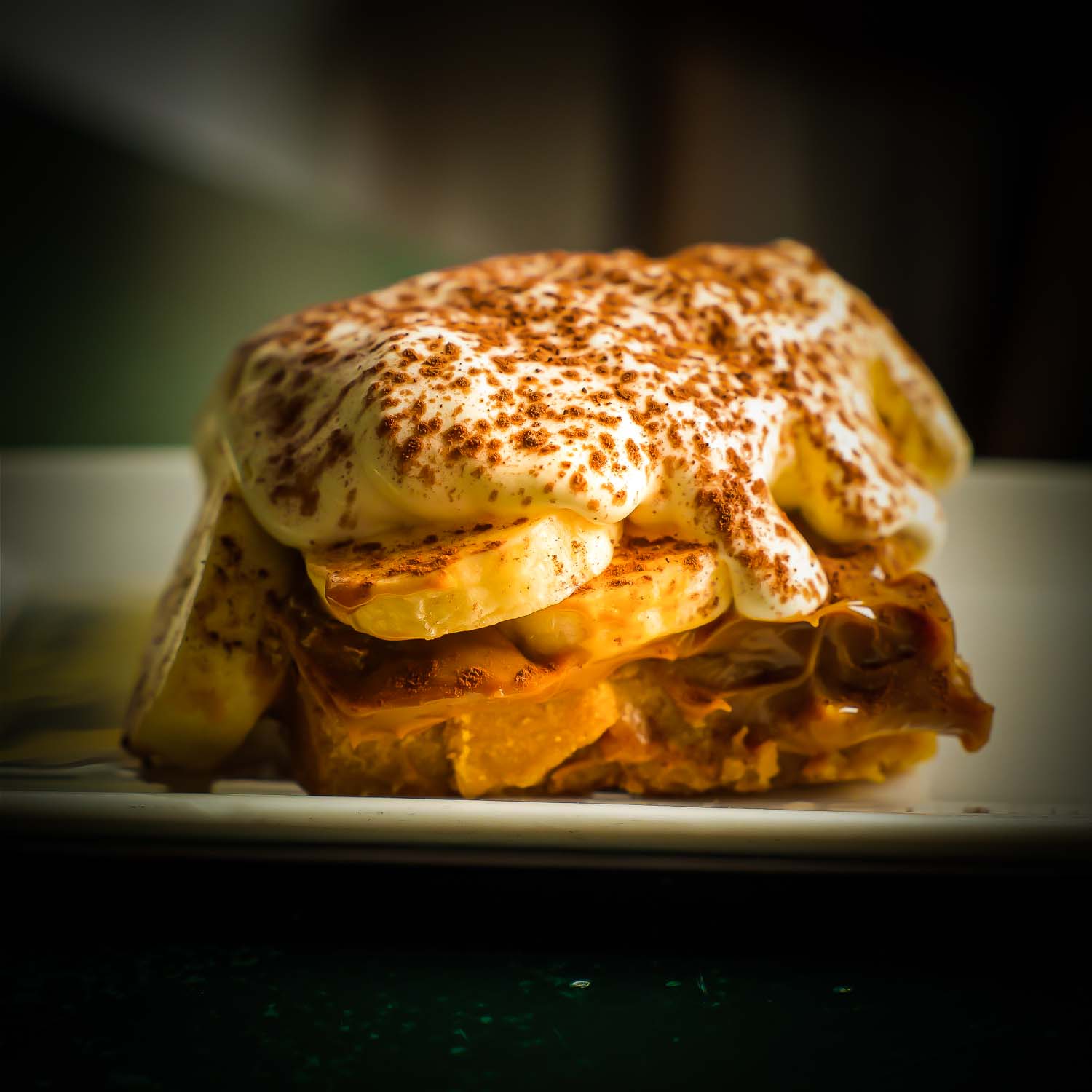 Slice of Banoffee pie with layers of banana, dulce de leche, and cream on a peanut-biscuit base