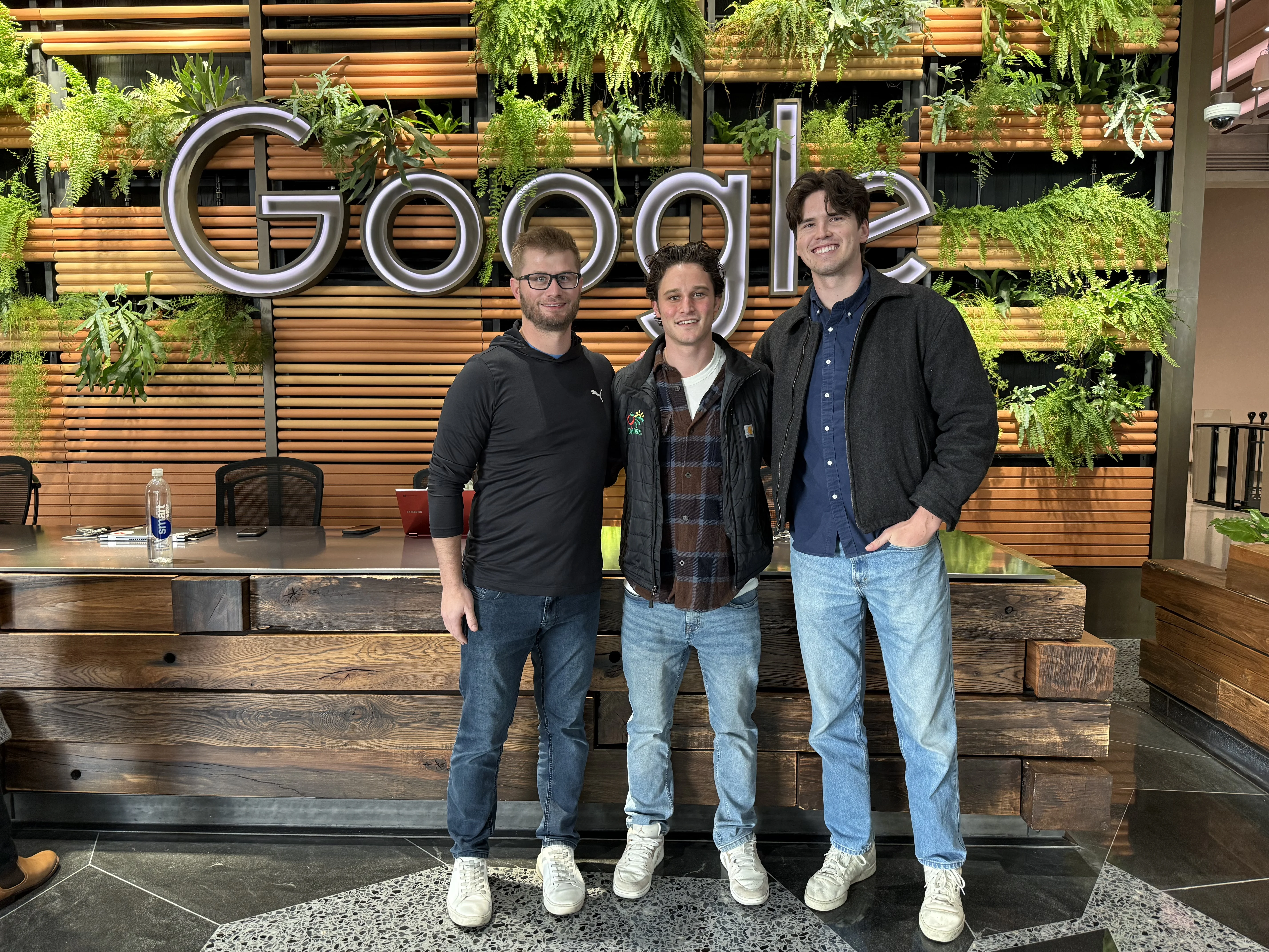 Three members of the Onward team standing in front of a Google logo plant wall