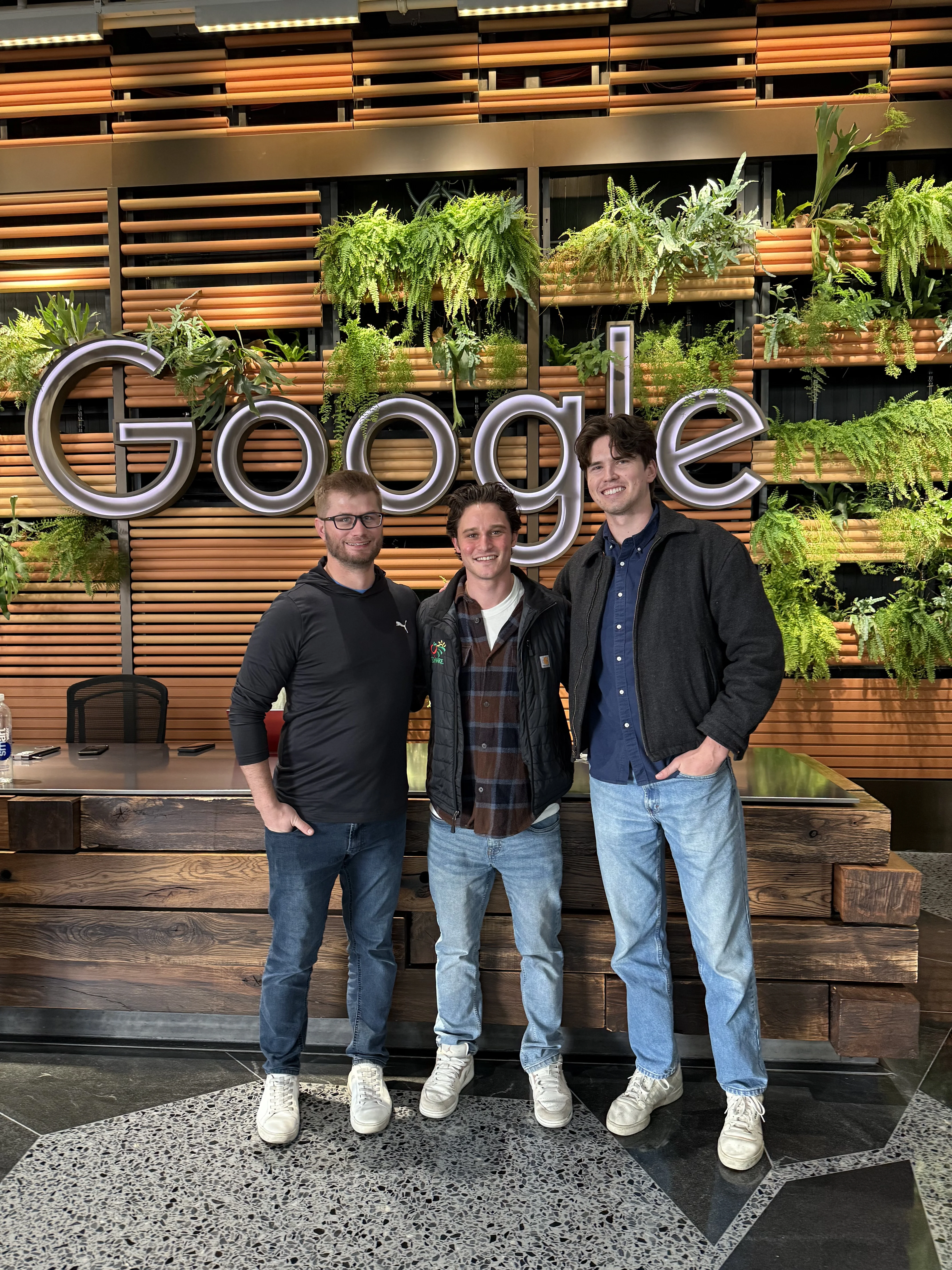 Three members of the Onward team standing in front of a Google logo plant wall