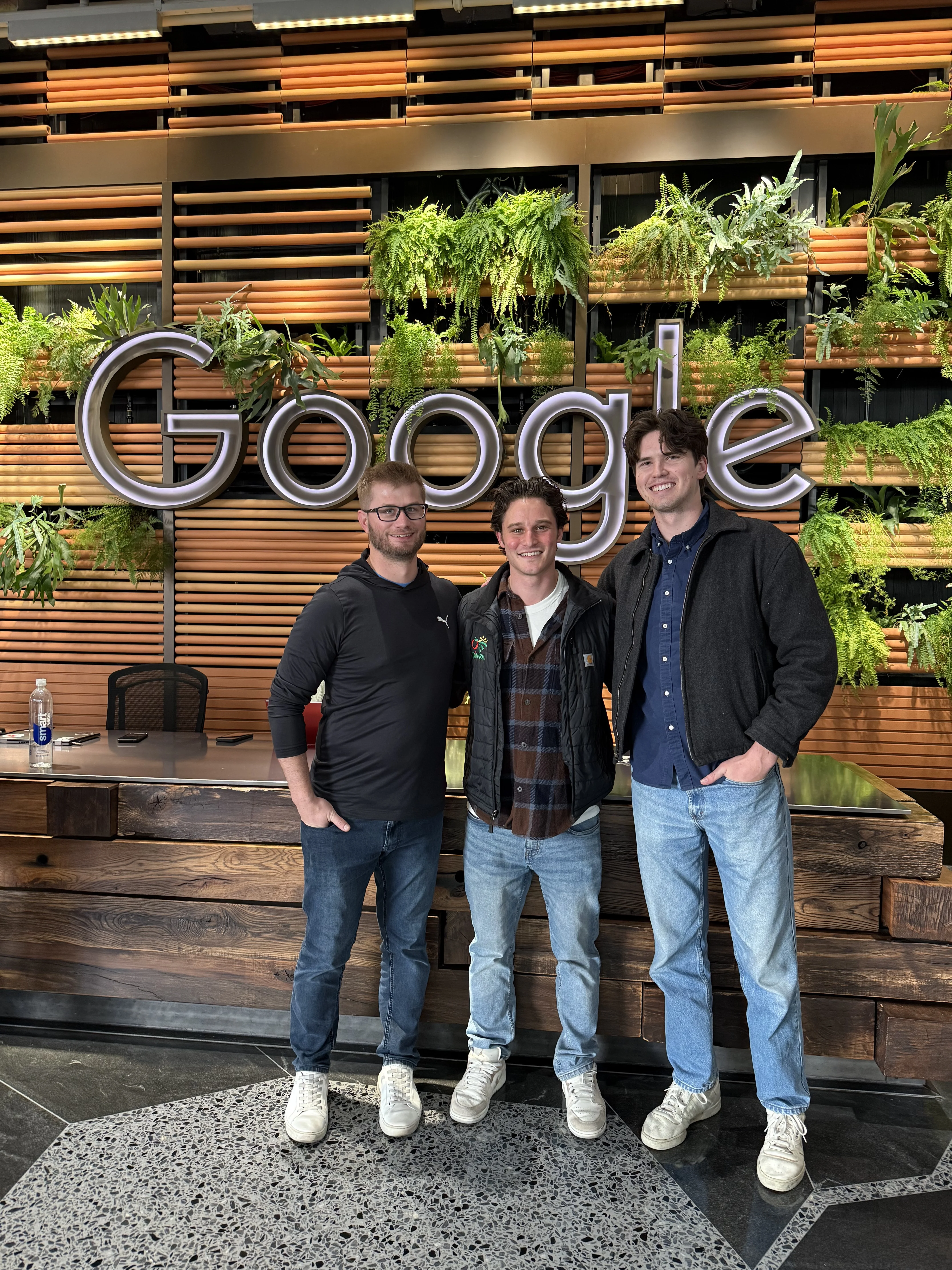 Three members of the Onward team standing in front of a Google logo plant wall
