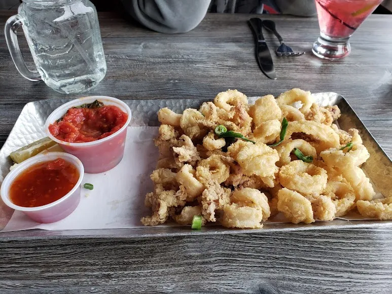 A tray of crispy fried squid served with a small bowl of dipping sauce.
