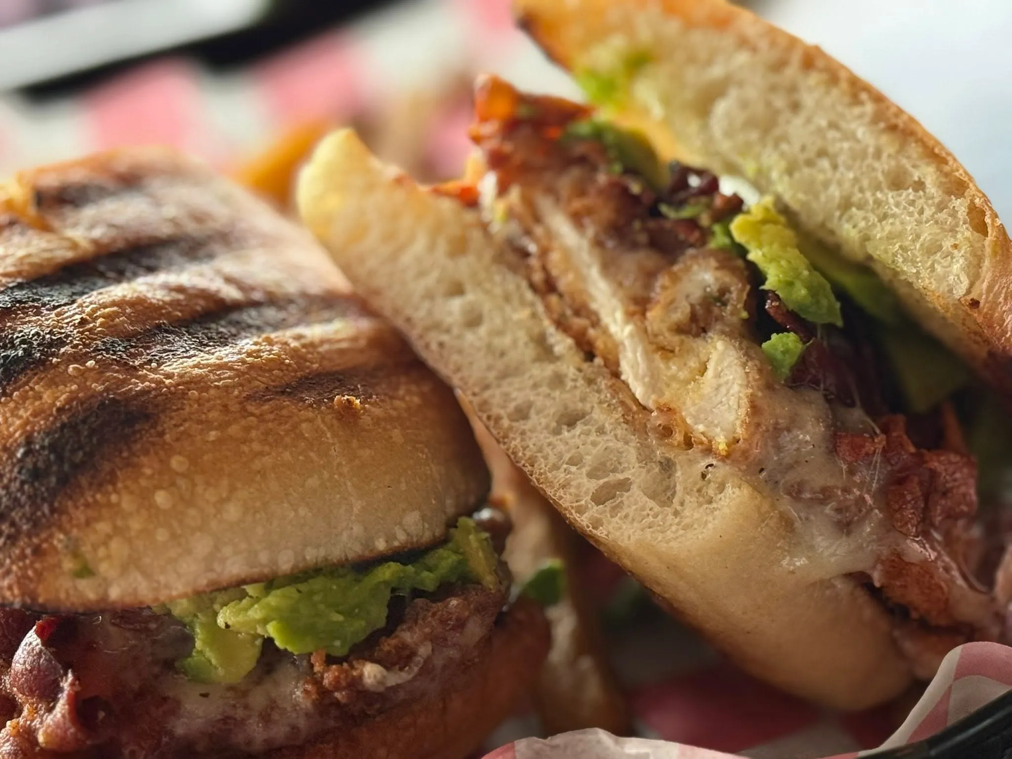 A sandwich filled with layers of meat, cheese, and fresh avocado slices on a toasted bread.
