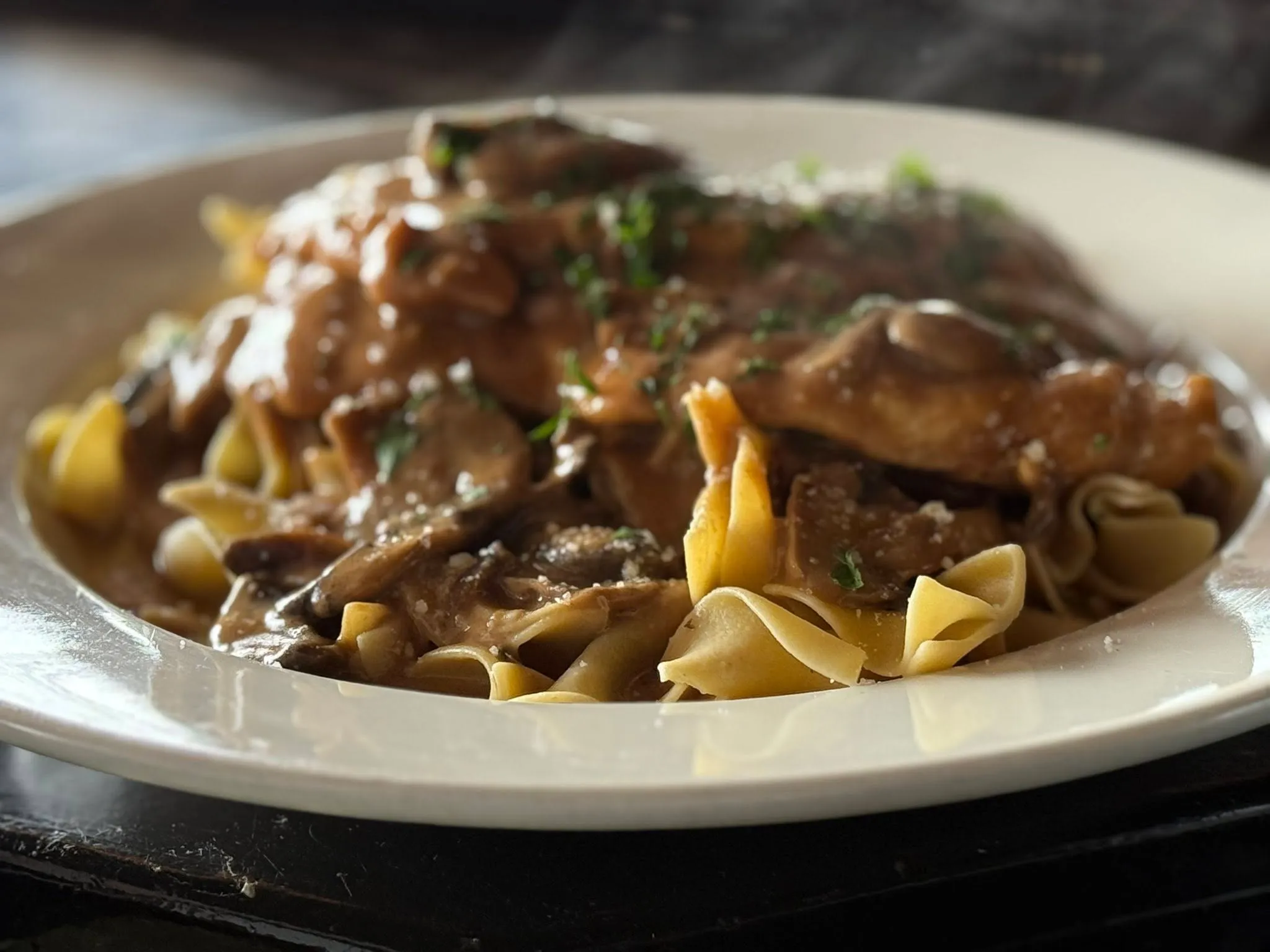 A plate of creamy chicken and mushroom pasta garnished with parsley, showcasing a delicious and hearty meal.