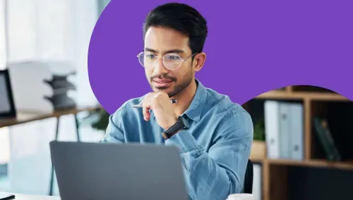 A man in glasses thoughtfully looking at a laptop screen in an office