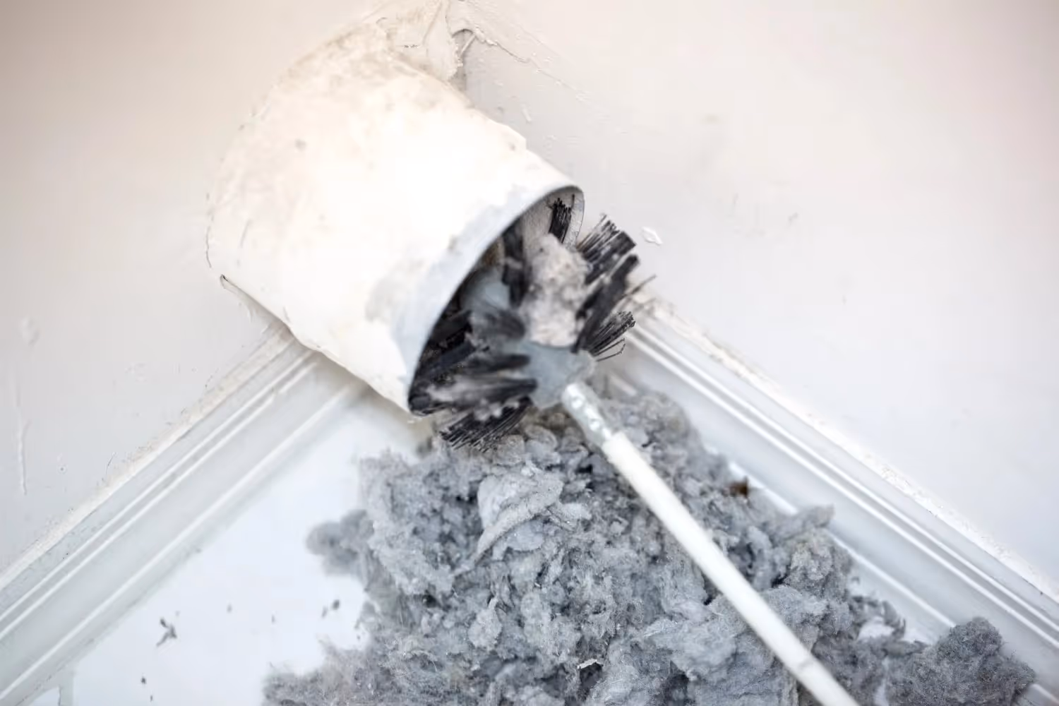 A large pile of gray lint being removed from a dryer vent pipe with a long brush.