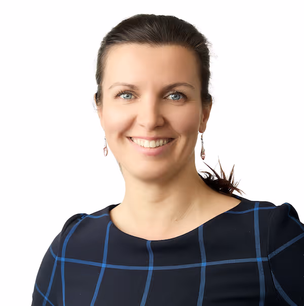 Usměvavá žena s modrýma očima, tmavými vlasy sepnutými dozadu a tmavým svetrem s modrými pruhy.