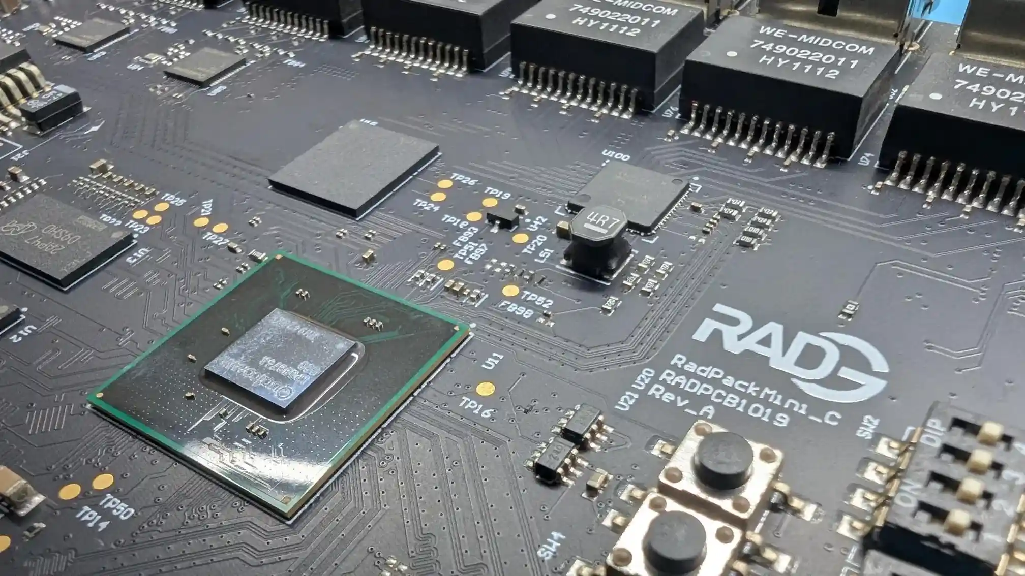 Close-up of a RADG electronic circuit board featuring integrated chips, surface-mounted components, buttons, and distinct printed text including 'RADG', 'RadPack Mini_C', and 'RADPCB1019 REV_A'.