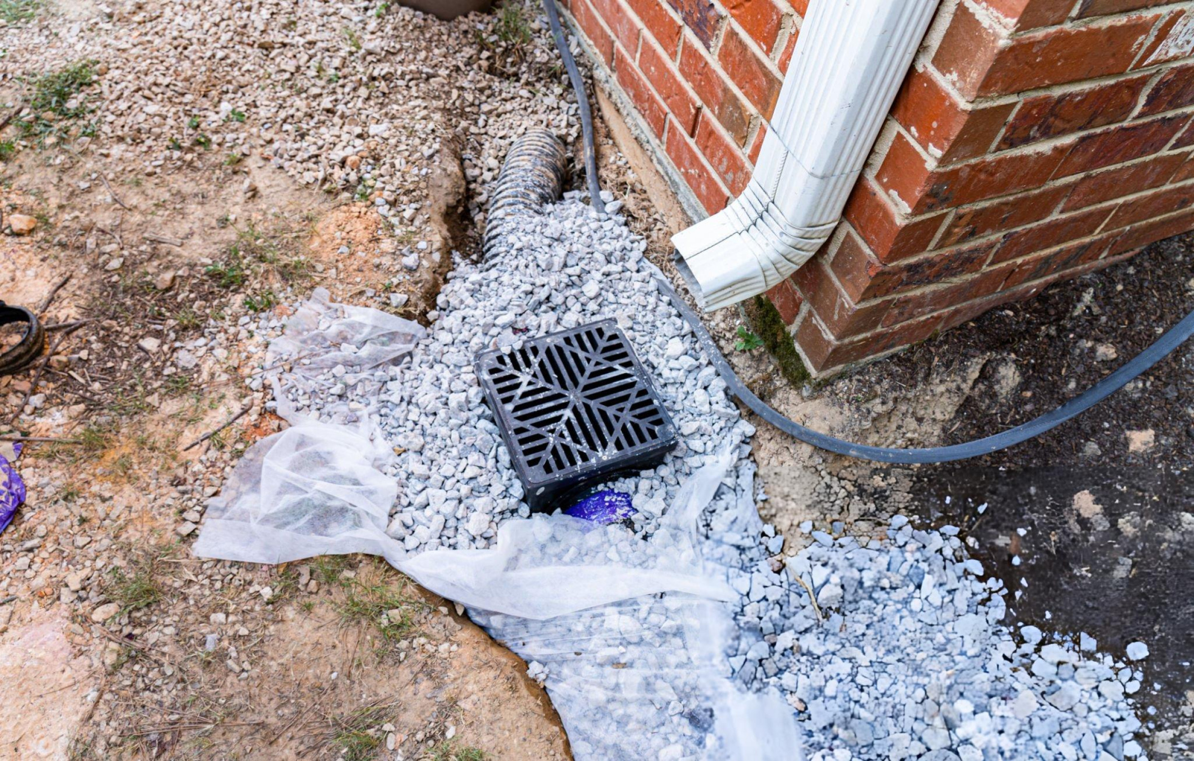 Landscape drainage solutions in DFW with catch basin and gravel drainage system beside a home