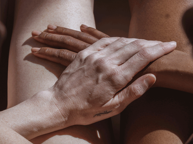 Overhead close-up of two people sitting closely together, their hands rested on top of each other in caring gesture.