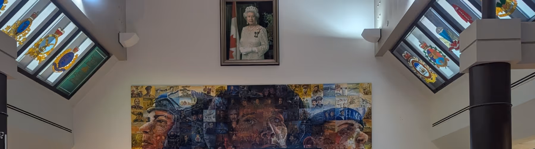 Interior wall with a framed portrait of Queen Elizabeth II above a large mural composed of many smaller images forming faces, flanked by angled light panels displaying military crests.