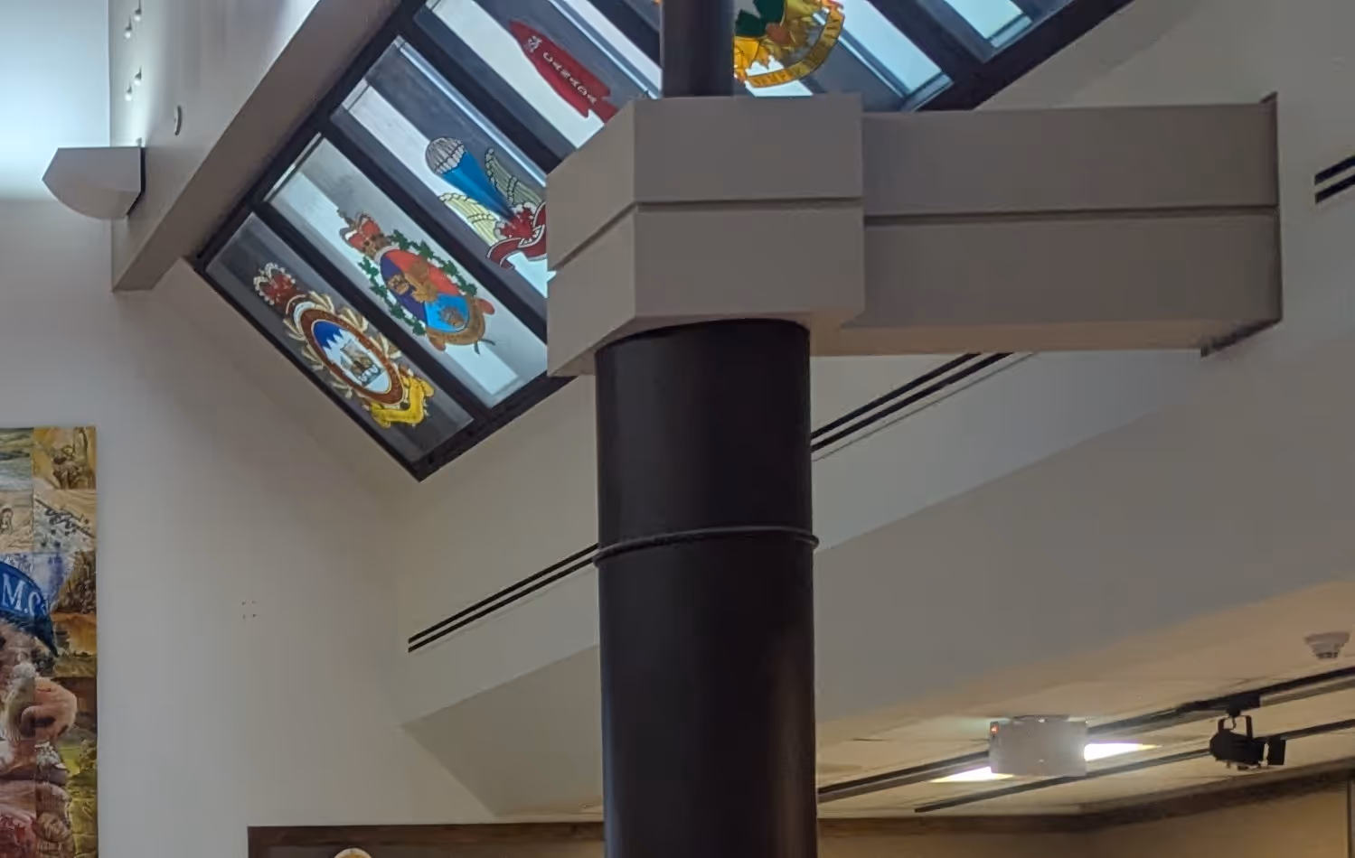 Interior with skylight windows featuring colorful stained glass coats of arms and a black column supporting a ceiling beam.
