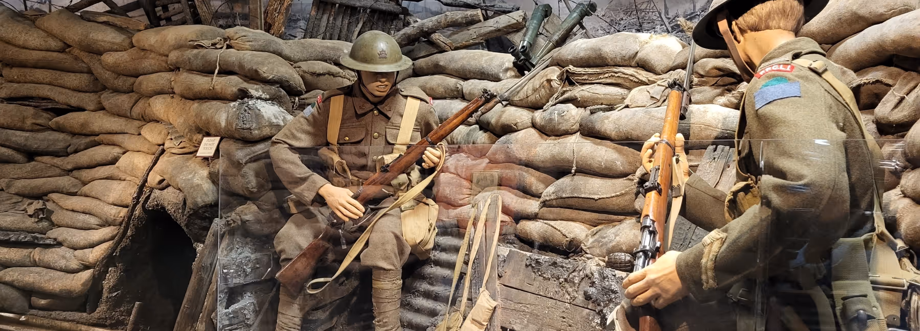 Museum diorama of two soldiers in World War I trench surrounded by sandbags, holding rifles.