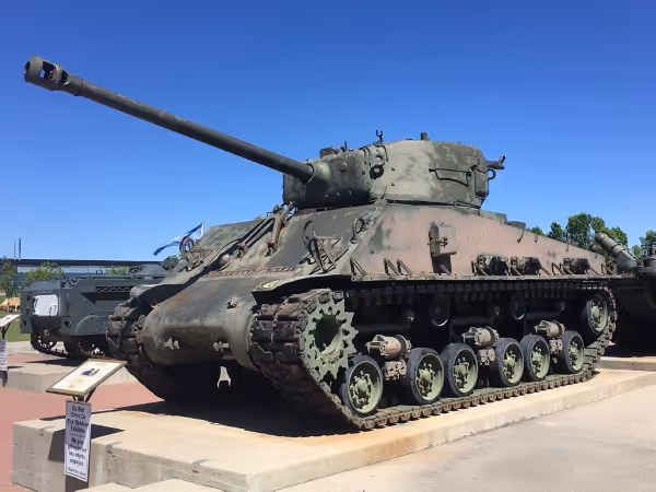 Green World War II-era military tank displayed outdoors on a concrete platform under clear blue sky.