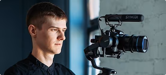 Young man operating a professional video camera with a mounted microphone.