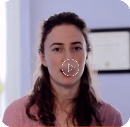Woman with long hair speaking in a softly lit room with a framed certificate on the wall behind her.