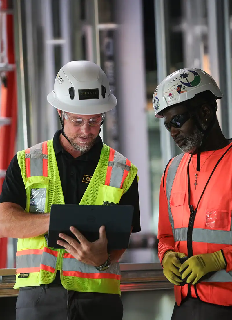 Two men in hard hats and construction vests looking at a tablet