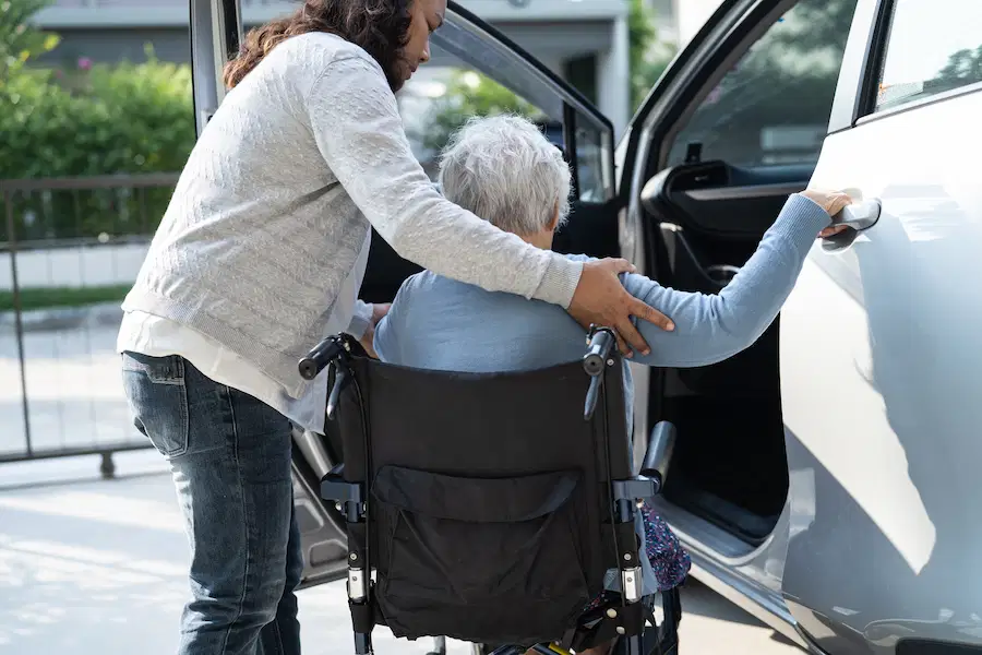 volunteer driving aiding senior into car from wheelchair