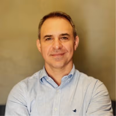 Homem de camiseta azul clara com braços cruzados e fundo neutro.