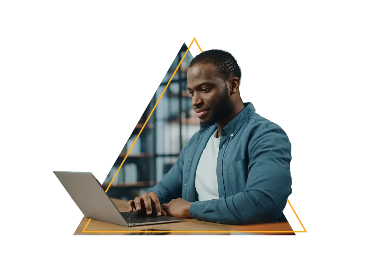 Homem negro sentado à mesa trabalhando em um laptop em um ambiente interno moderno.