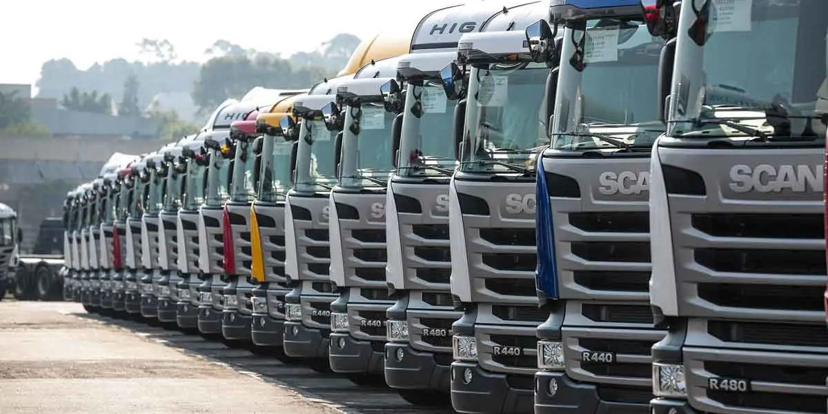 Fila de caminhões Scania estacionados lado a lado em um pátio aberto.