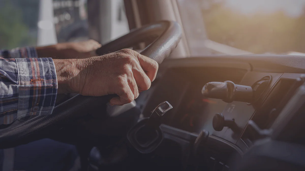 Mãos de um motorista segurando o volante de um caminhão durante o dia.