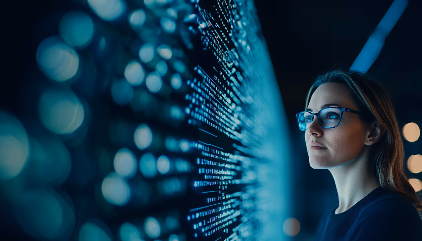 Mulher de óculos olhando atentamente para código digital azul em uma tela grande escura.
