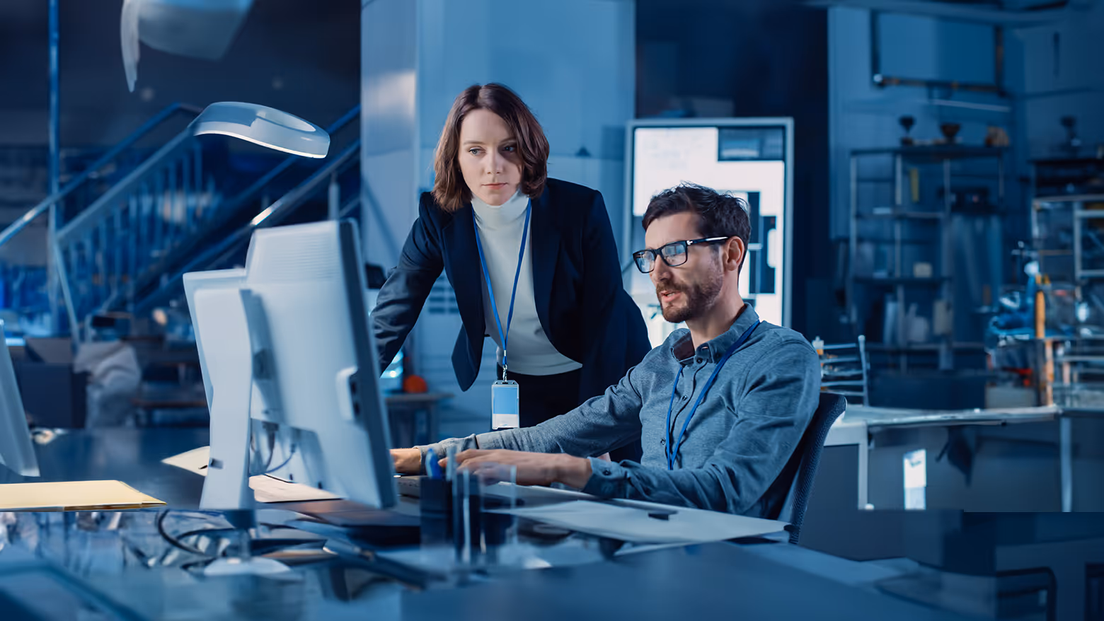 Homem sentado e mulher em pé discutindo enquanto olham para um computador em um escritório moderno.