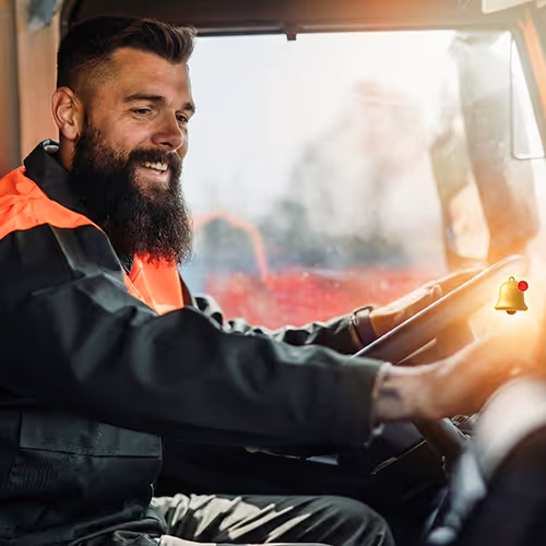 Homem sorridente dirigindo um caminhão, usando uniforme de trabalho preto com detalhes laranja.