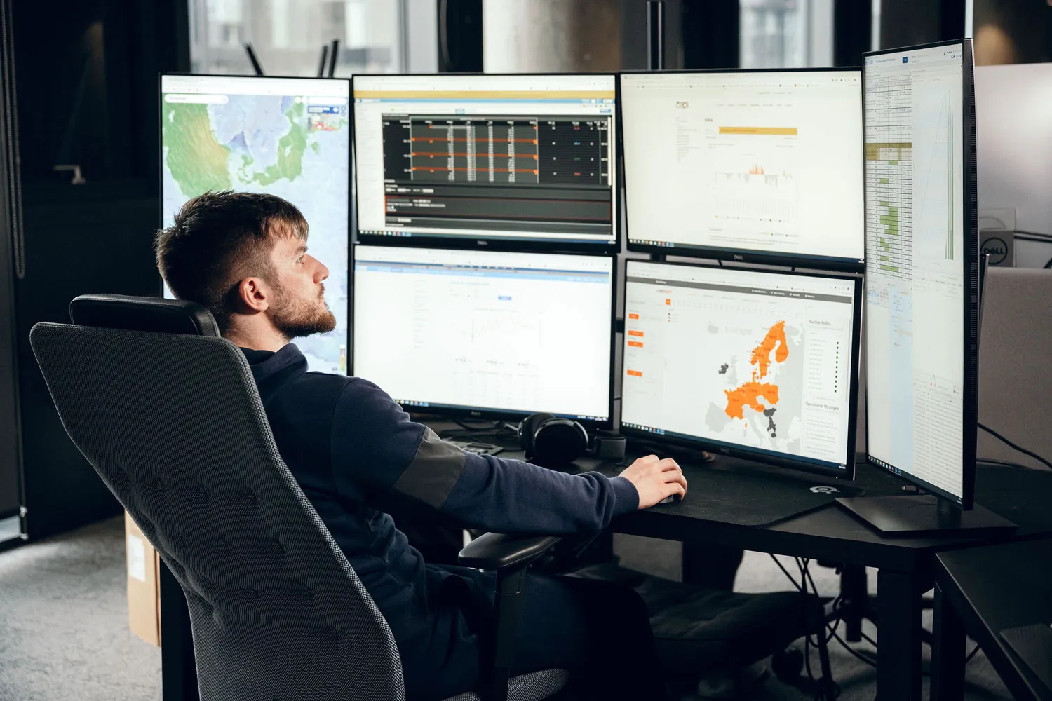 Data analyst working at multi-monitor setup with maps and charts displayed