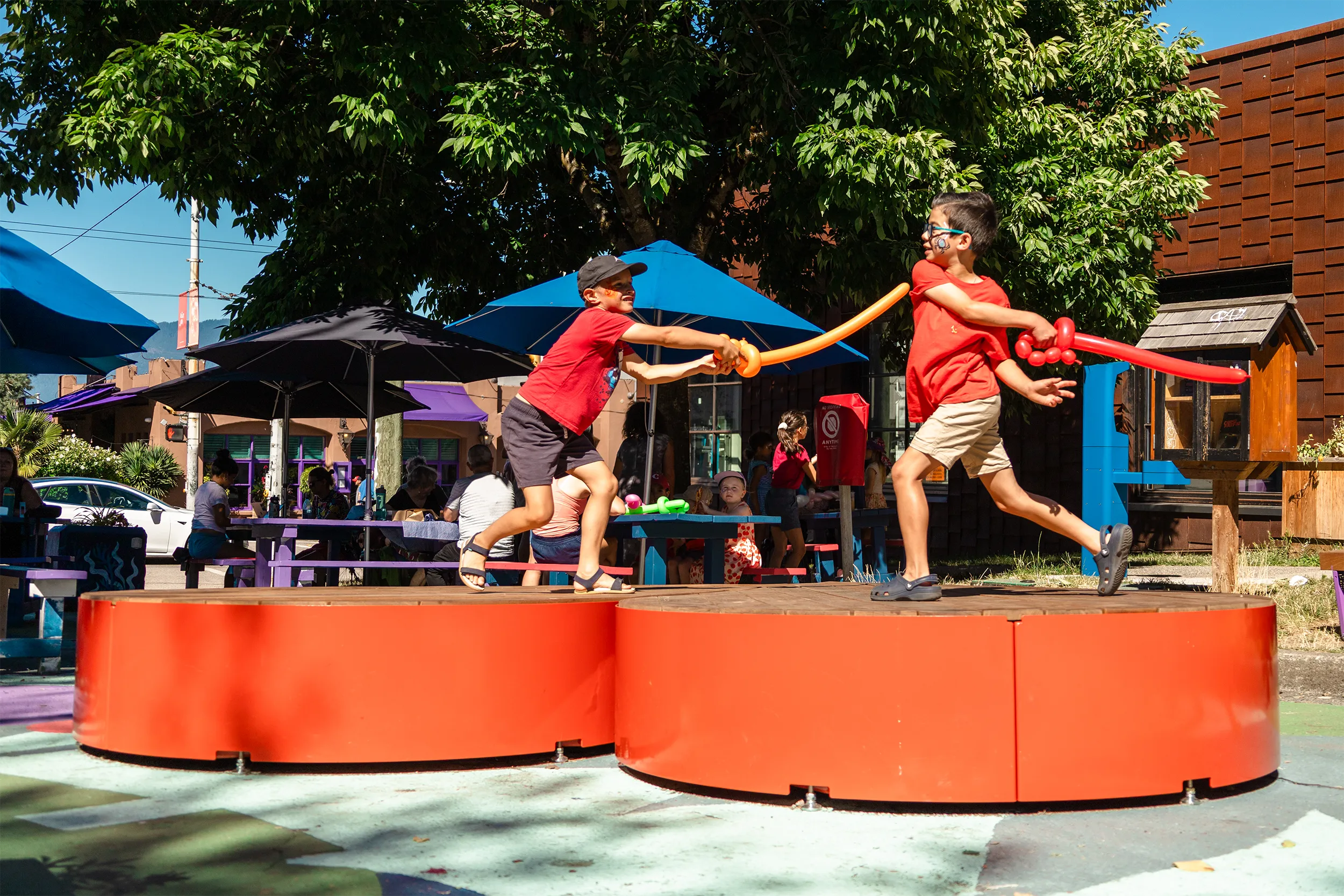 Two kids duelling with balloon swords on top of a large, heart-shaped bench