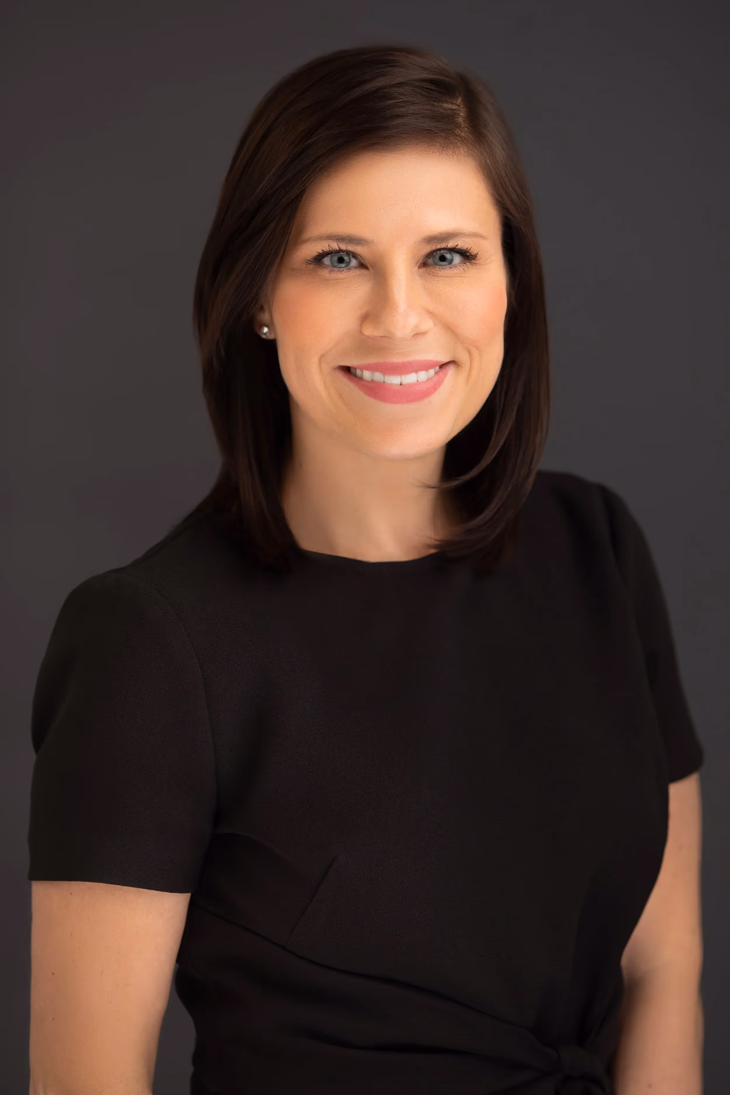 Professional headshot of a smiling woman in black shirt against gray background