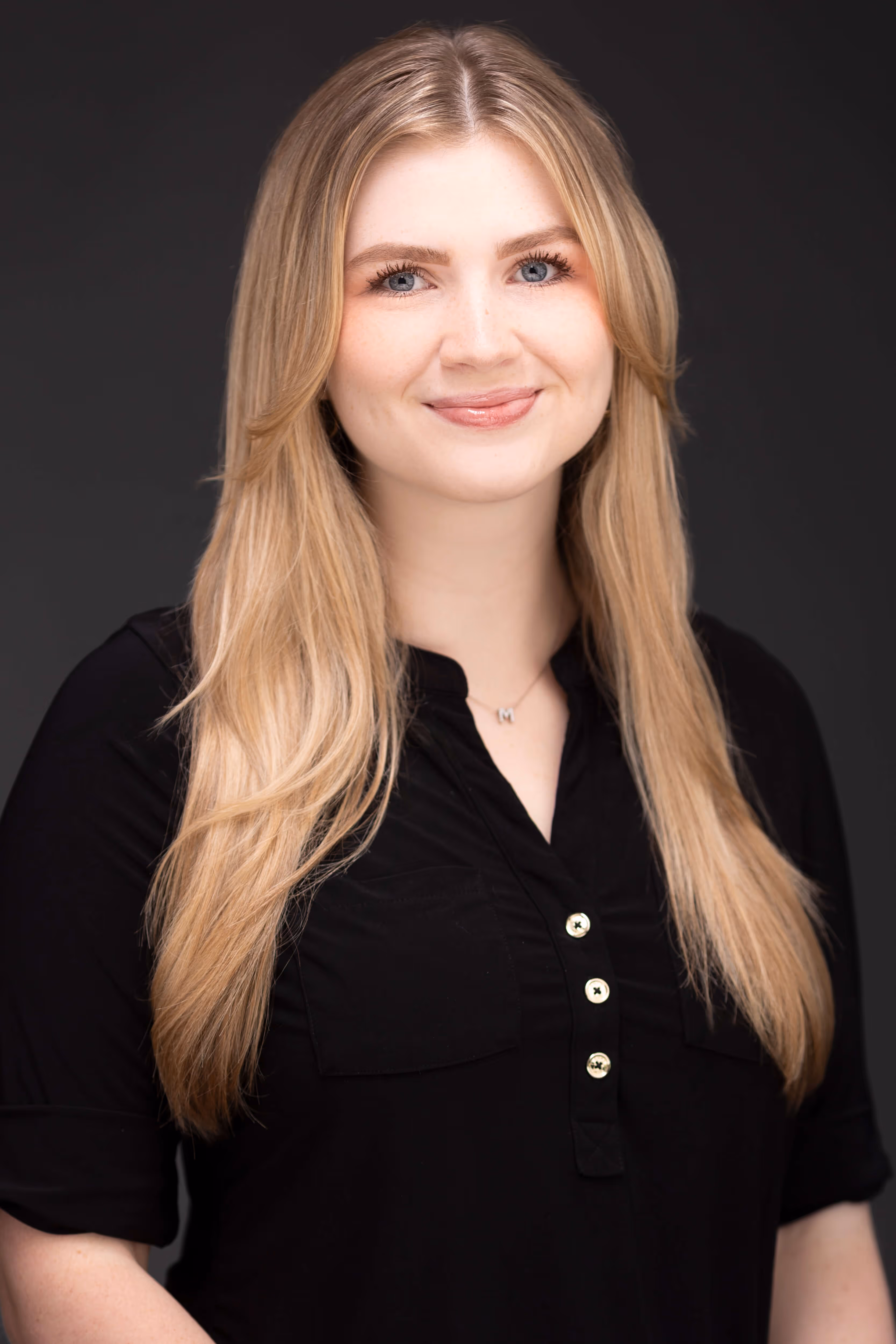 A woman with long blonde hair smiles in a black buttoned shirt
