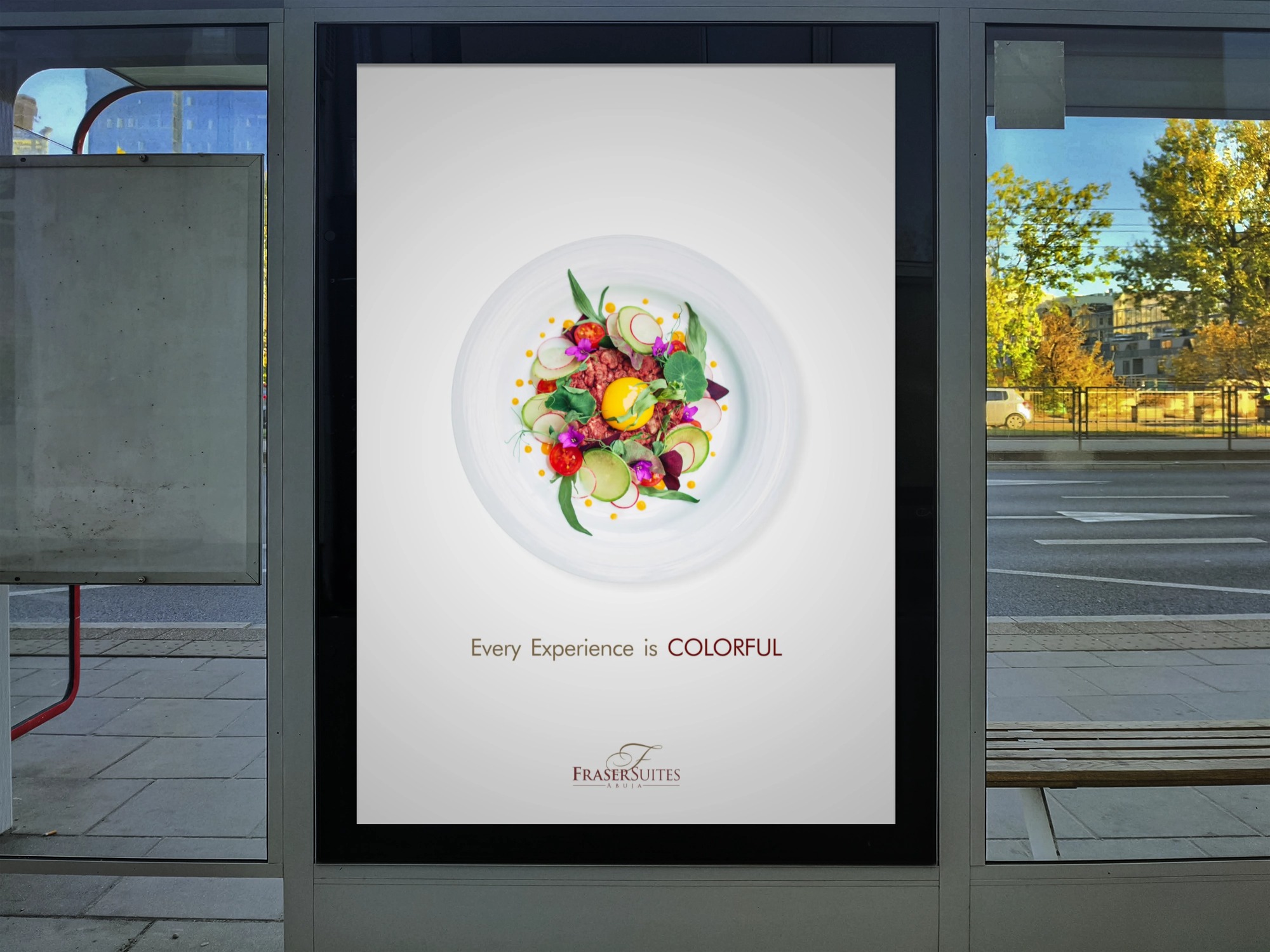 Advertising display showing a white plate with colorful gourmet food and text 'Every Experience is COLORFUL' above 'Fraser Suites Abuja' logo.